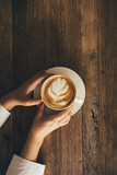 Female hands holding white cup with cappuccino on wooden background.