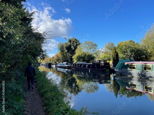 Rear view of a man walking along a towpath and Narrowboats moored along Grand Union Canal, Bourne End, Hertfordshire, England, UK photo