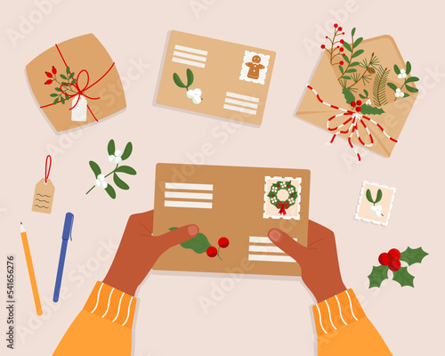 Hands holding an envelope with stamps surrounded by stationery. Top view of the table surface. Sending a letter or correspondence by post. Christmas mail. Vector illustration