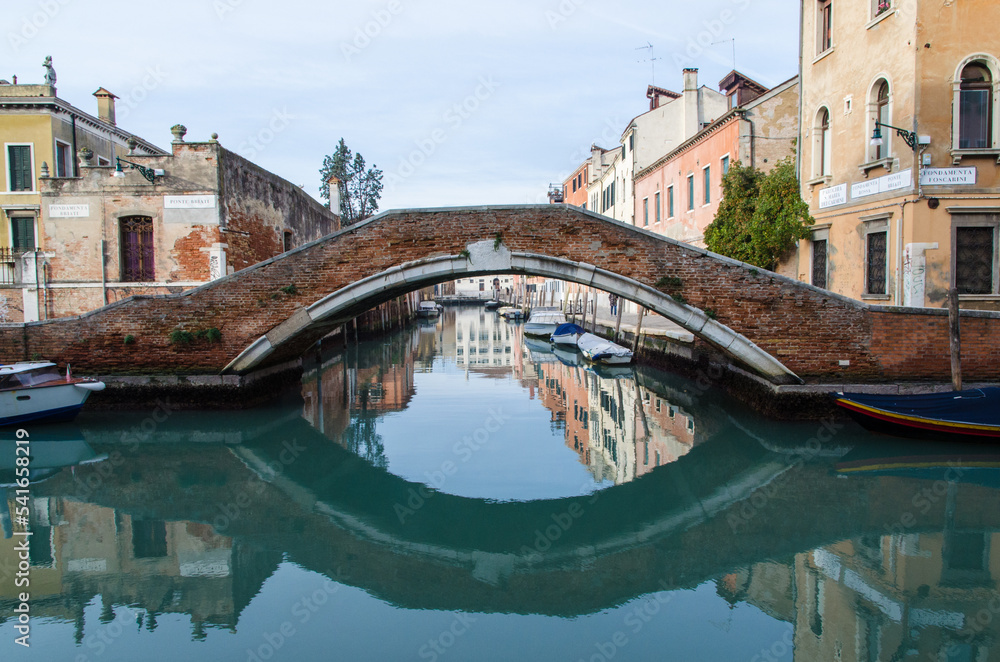 Un ponte attraversa un canale di Venezia e si riflette nell'acqua calma
