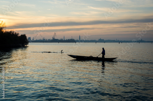 La silhouette di un uomo che voga in piedi sulla sua barca il tramonto e Venezia sullo sfondo