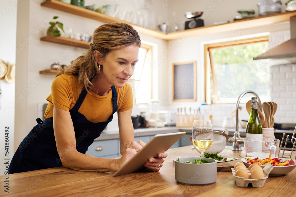 Woman, tablet and kitchen for online recipe, browsing or research in cooking or baking at home. Female with apron checking instructions on the internet for meal or ingredients on touchscreen indoors