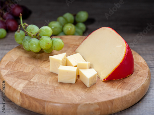 Edam cheese on wooden cutting board with grapes