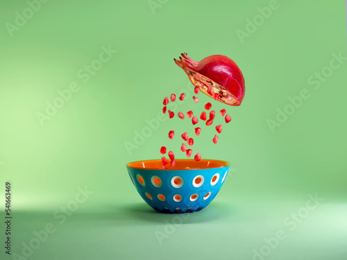 Halved pomegranate with pomegranate seeds falling into a bowl that looks like a pomegranate photo