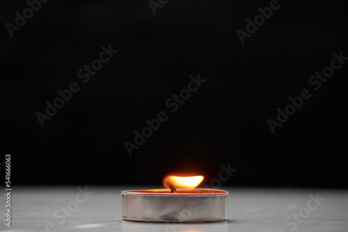 A candle made of red paraffin in an aluminum case stands on the table. Back black background. A lonely burning candle. Selective selective focus