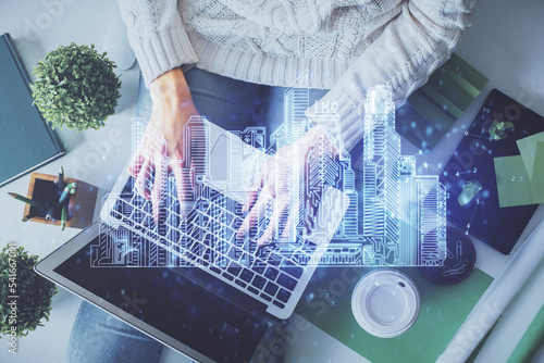 Double exposure of woman hands working on computer and buildings construction hologram drawing. Top View. smart city concept. photo