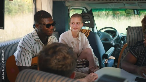 Young adult group of friends sitting inside camper van parked in field relaxing and having friendly conversation. Horizontal video. High quality 4k footage