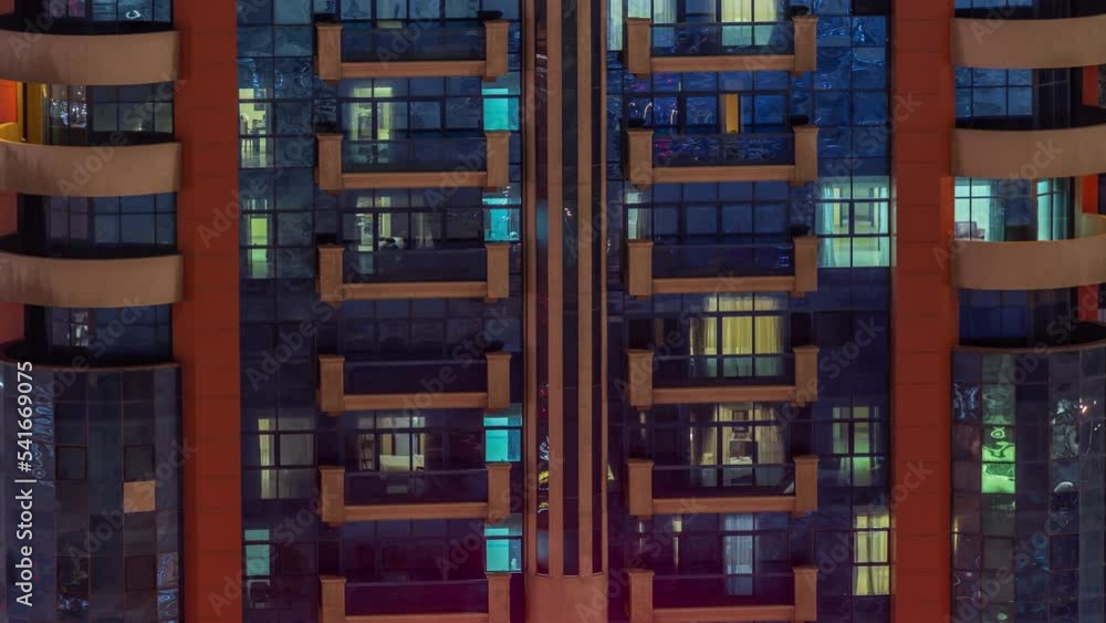 Night aerial view of apartment building glass window facade with illuminated lighted workspace rooms timelapse. Glowing light in skyscraper with glass surface Night aerial view of apartment building glass window facade with illuminated lighted workspace rooms timelapse. Glowing light in skyscraper with glass surface