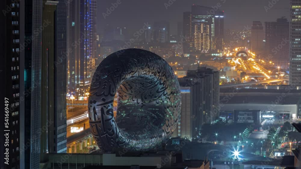 Museum of the Future exhibition space aerial during all night timelapse with iconic torus shape with lights turning off. Facade of stainless steel and windows that form an Arabic poem