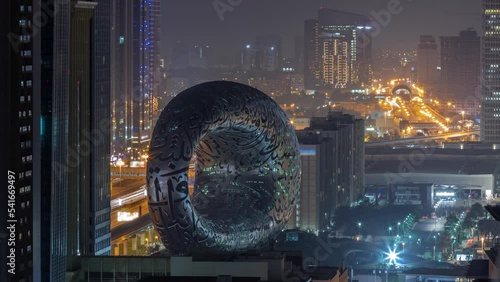 Museum of the Future exhibition space aerial during all night timelapse with iconic torus shape with lights turning off. Facade of stainless steel and windows that form an Arabic poem photo
