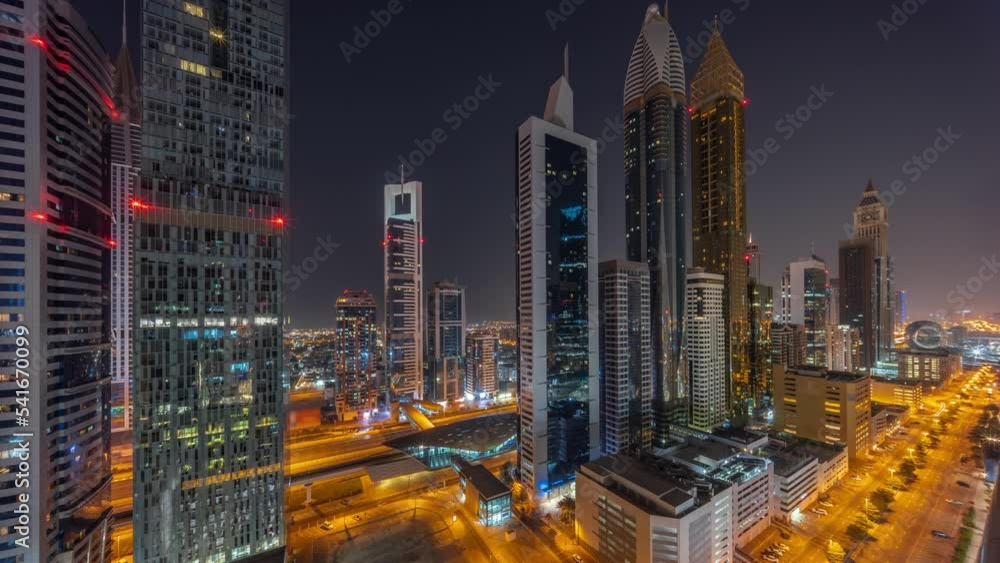 Aerial view of Dubai International Financial District with many skyscrapers during all night timelapse with lights turning off. Traffic on a road near multi storey parking with rooftop swimming pool Aerial view of Dubai International Financial District with many skyscrapers during all night timelapse with lights turning off. Traffic on a road near multi storey parking with rooftop swimming pool