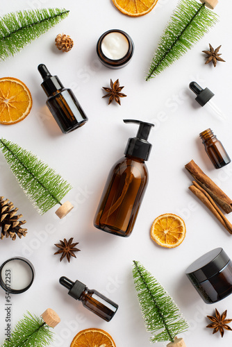 Organic cosmetics concept. Top view vertical photo of amber pump bottle cream jars dropper bottles pine cones cinnamon sticks dried orange slices anise christmas tree toys on isolated white background