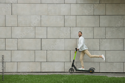 Businessman riding modern kick scooter near grey stone wall outdoors, space for text photo
