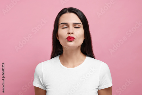 Beautiful young woman giving kiss on pink background