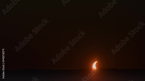 Solar eclipse at sunset. The sun, like a sun-covered moon, sets in a lake. Siberia, October 25, 2022.
