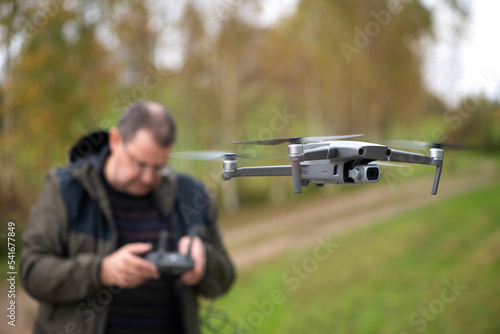 Mature man operating drone flying or hovering by remote control in nature