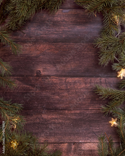 Wooden dark Christmas background, spruce branches with garland lights, space for text, flat layout.