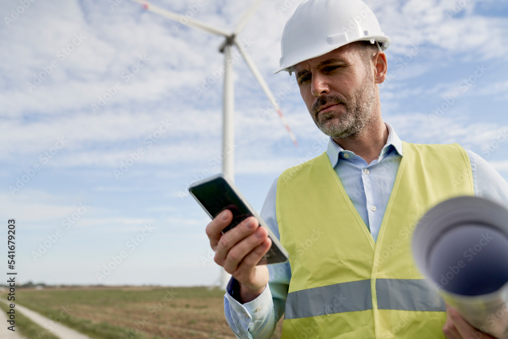 Caucasian male engineer standing on wind turbine field and using mobile phone Caucasian male engineer standing on wind turbine field and using mobile phone