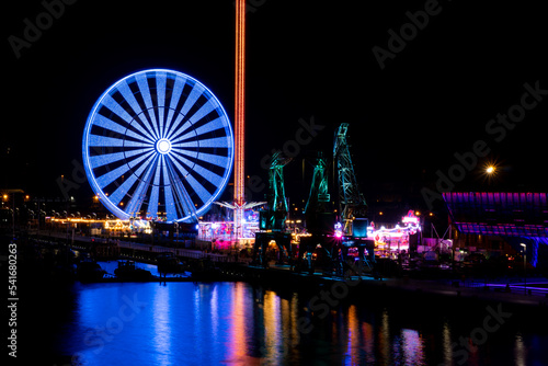 Colorful Szczecin by the river Oder at night. City at night and neon lights, ferris wheel and bridge. Poland, summer 2022 