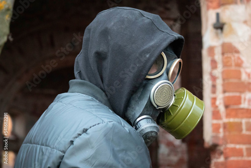 The guy in the gas mask looks over his shoulder. Photo of guy in black jacket and black hood protecting his breath from gases and radiation