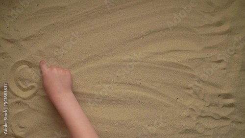 the child writes a word on the sand with his finger. the word chuffed. slow motion video