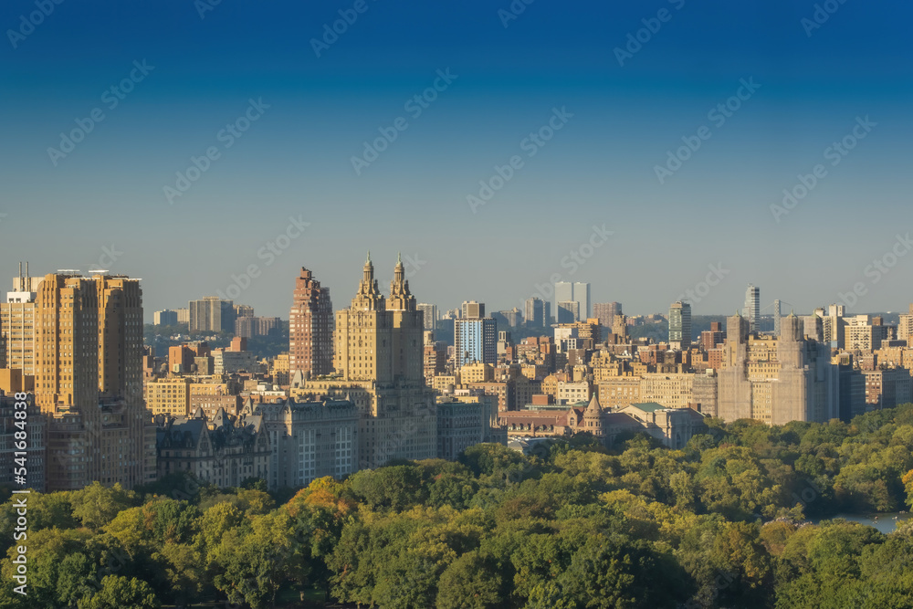 Fototapeta premium Aerial view of the Central park in Manhattan, New York with golf fields and tall skyscrapers surrounding the park. Sunset view.