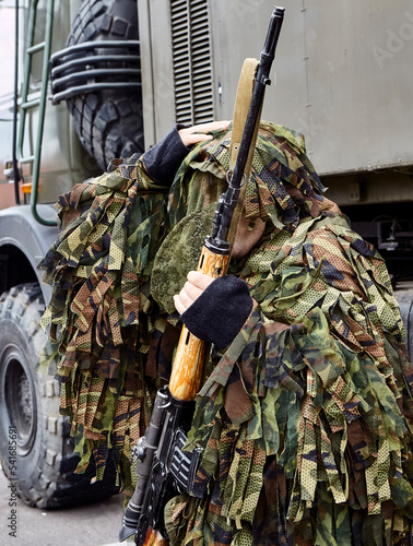 Close-up portrait of a military sniper in camouflage green army clothes with a Degtyarev sniper rifle in his hand. photo