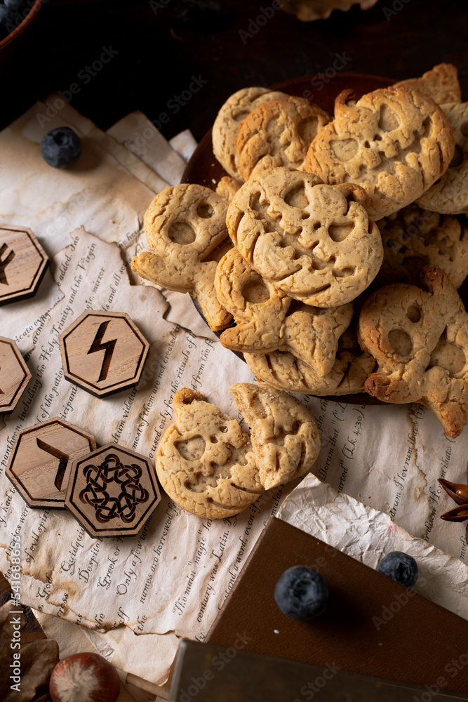 Runes lie on a wooden table next to cookies in the form of pumpkins and ghosts Runes lie on a wooden table next to cookies in the form of pumpkins and ghosts