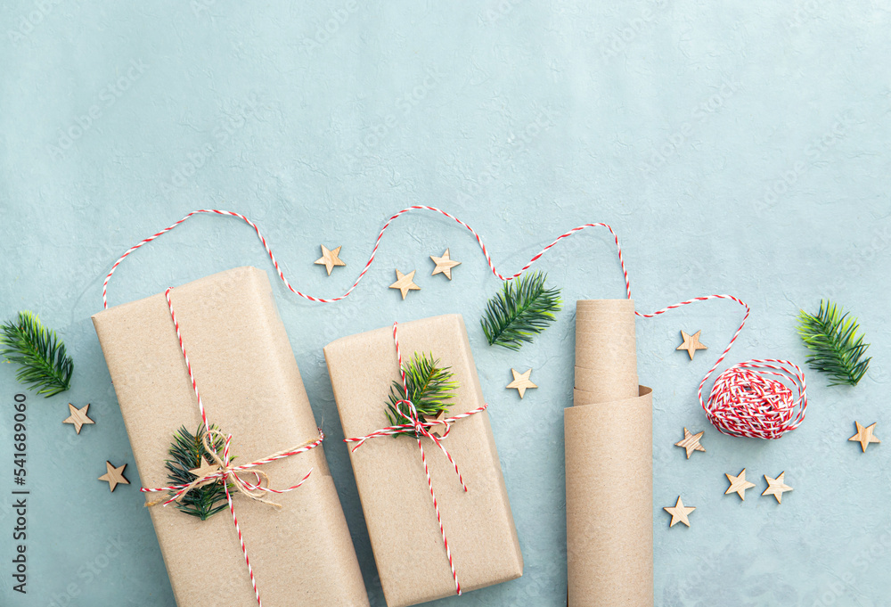 Gift wrapping with natural brown packing paper called Sack kraft paper or sack paper. Gifts decorated with red and white paper string , small wood stars and fir tree branch on blue background. Gift wrapping with natural brown packing paper called Sack kraft paper or sack paper. Gifts decorated with red and white paper string , small wood stars and fir tree branch on blue background.