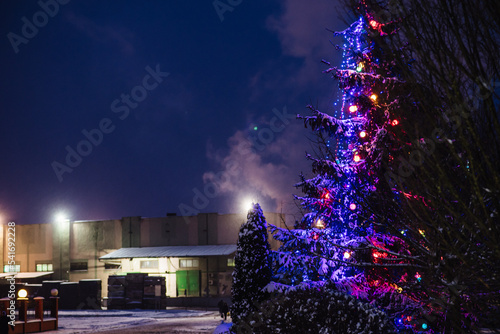 Christmas tree in a snowy city at night. Smoke from the chimney of a large enterprise envelops the snowy city. The concept of a warm winter in Ukraine and Europe.
