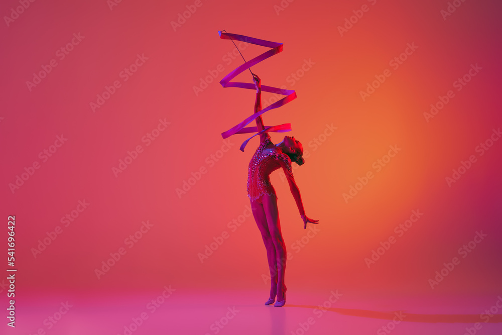 Young flexible teen girl rhythmic gymnast in motion, action isolated over pink background in neon light. Sport, beauty, competition, flexibility, active lifestyle - obrazy, fototapety, plakaty 