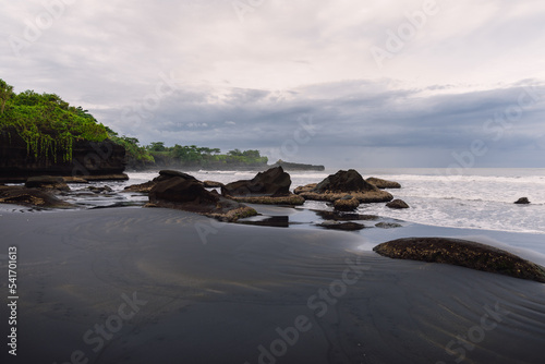 Volcanic sandy beach with ocean and waves in Balian. Beach with rocks and cloudy sky