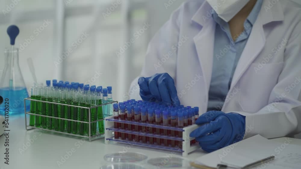 A female scientist doing chemistry experiments in a laboratory.A beautiful woman doctor in a hat and mask pours a solution from a test tube onto a glass bottle containing red and green liquid. A female scientist doing chemistry experiments in a laboratory.A beautiful woman doctor in a hat and mask pours a solution from a test tube onto a glass bottle containing red and green liquid.