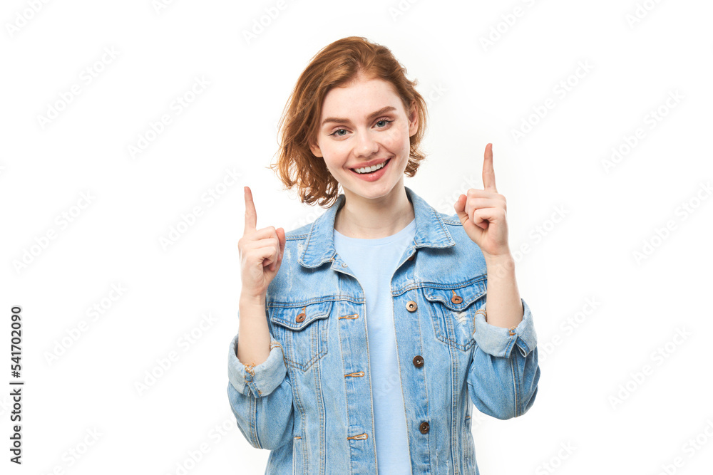 Portrait of positive redhead young woman in casual jeans smiling pointing with finger at empty copy space for text or product isolated on white background, advertising banner Portrait of positive redhead young woman in casual jeans smiling pointing with finger at empty copy space for text or product isolated on white background, advertising banner