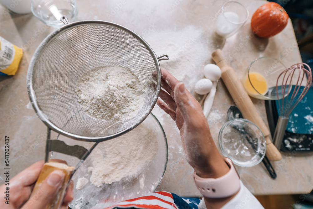 Woman's hands sifting flour through sieve. Selective focus.