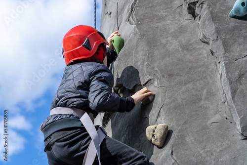 Kid in helmet having fun at bouldering wall. Teen boy at outdoor climbing wall. Sports healthy lifestyle. Sport weekend action in adventure park.