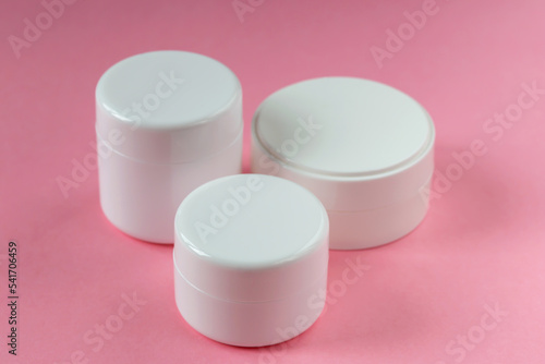 Three white cosmetic jars on a pink background