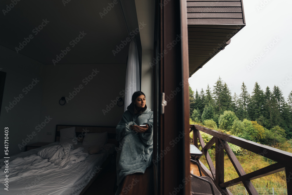 Woman sits on the windowsill and looks at the mountains