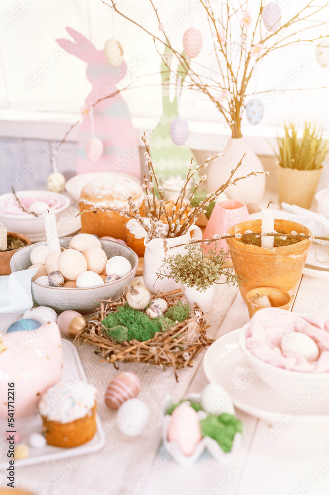 happy easter and spring holidays time. festive tablescape set decor. traditional dinner food easter eggs and baked cakes on table at home. rabbit and willow. pale pop pastel blue and pink color. flare