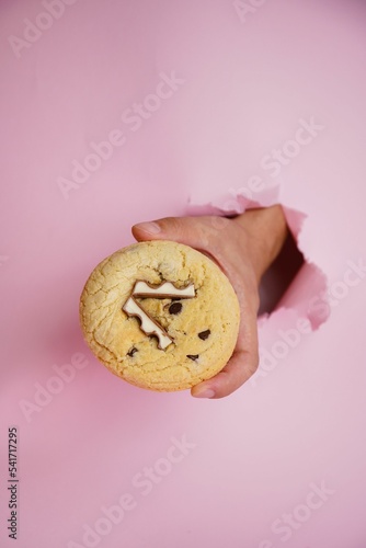 Hand holding chocolate bar cookie on the pink background, vertical
