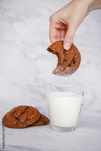 Chocolate cookie soaked in a cup of milk for breakfast, vertical