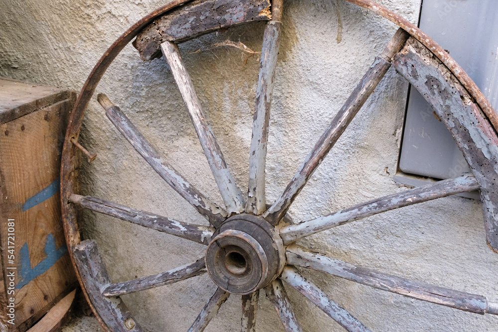 Old wagon wheel in a barn, a wooden carriage wheel against the wall, west handmade old wheel from the cart, a rustic and rural background, simple retro and vintage machine wheels.