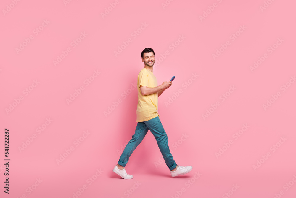 Full length profile side photo of good looking cheerful man go empty space read twitter facebook isolated on pink color background
