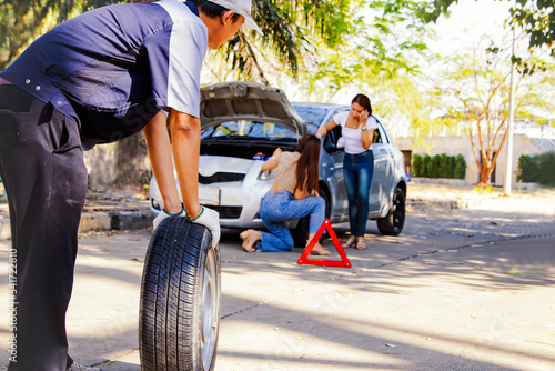 Onsite emergency service mechanic changing tires while traveling : Two women's hard work standing together to change a tire on a difficult road is to seek help from a mechanic.