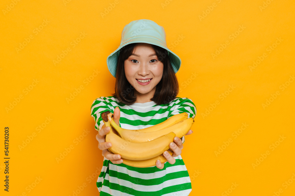 Asian young woman wearing panama smiling while holding bananas Asian young woman wearing panama smiling while holding bananas
