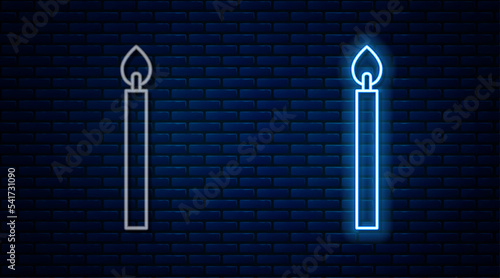 Glowing neon line Burning candle icon isolated on brick wall background. Cylindrical candle stick with burning flame. Vector
