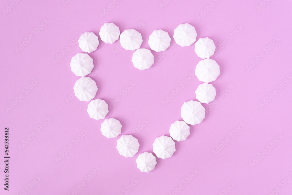 A heart formed by white meringues on a pink background, top down view.