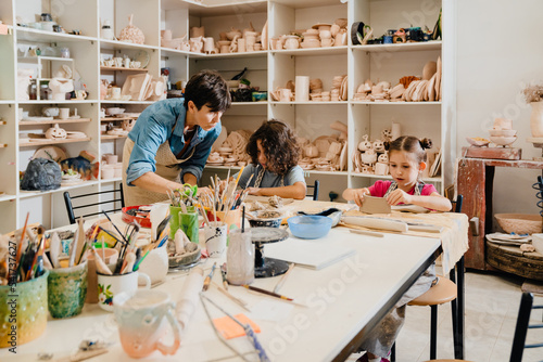 Mature female teacher working with group of kids in pottery workshop