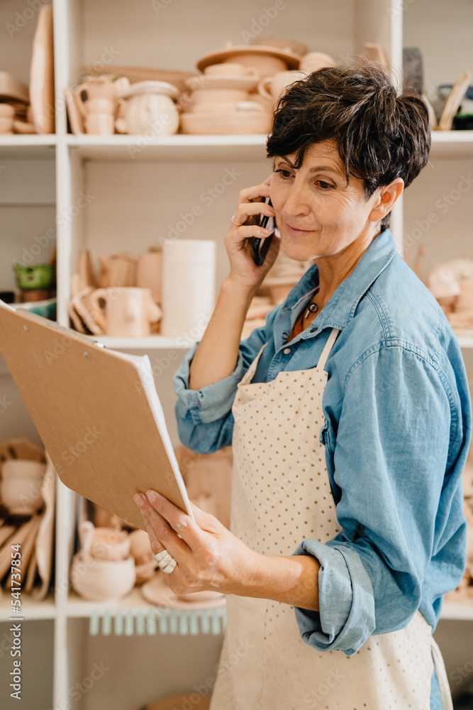 Mature woman talking on cellphone while working at the workshop Mature woman talking on cellphone while working at the workshop