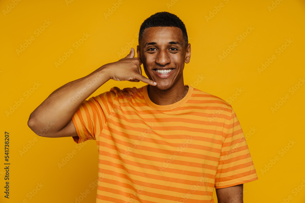 Afro man in striped orange shirt smiling and doing call gesture while standing isolated Afro man in striped orange shirt smiling and doing call gesture while standing isolated